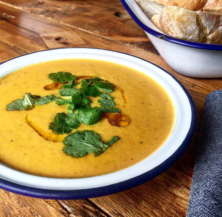 White enamel bowl filled with carrot and coconut soup, served with fresh coriander and baguettes
