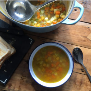 Bowl of vegetable soup next to a large saucepan of soup and a ladle