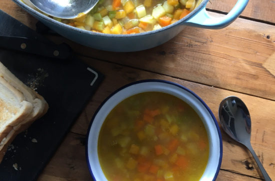 Bowl of vegetable soup next to a large saucepan of soup and a ladle