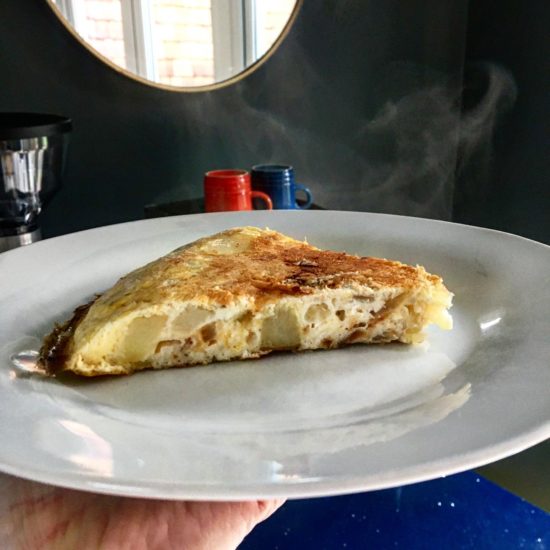 Wedge of potato and onion spanish omelette, served on a white plate.