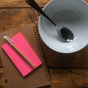 Notebook, post-its, pen and an empty soup bowl on a wooden table