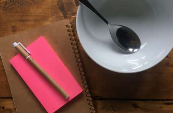 Notebook, post-its, pen and an empty soup bowl on a wooden table