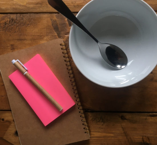 Notebook, post-its, pen and an empty soup bowl on a wooden table