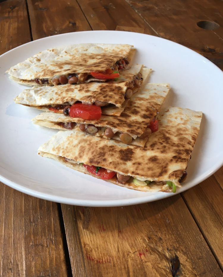 Bean, cheese and pepper quesadilla cut into  four pieces and served on w white plate