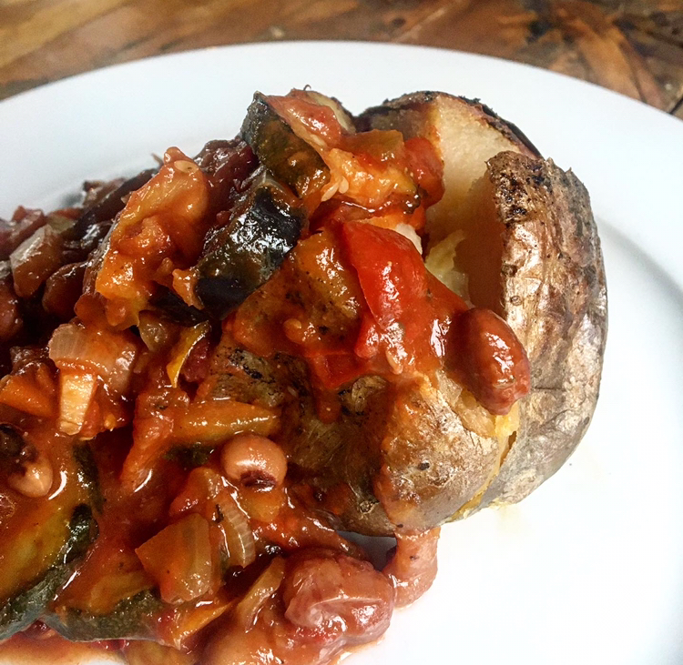 Vegetable chilli served over a slowcooked baked potato, on a white plate