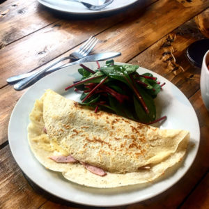 Cheese and ham filled savoury crepe with a beetroot side salad served on a white plate on a wooden slated table
