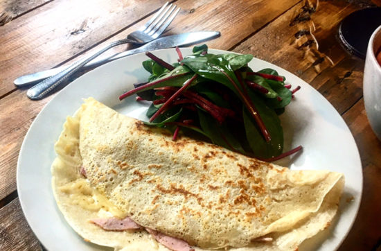 Cheese and ham filled savoury crepe with a beetroot side salad served on a white plate on a wooden slated table