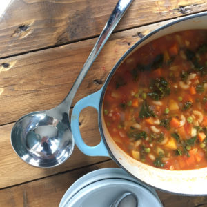 Large cast iron pan of minestrone soup, next to a ladle and bowls