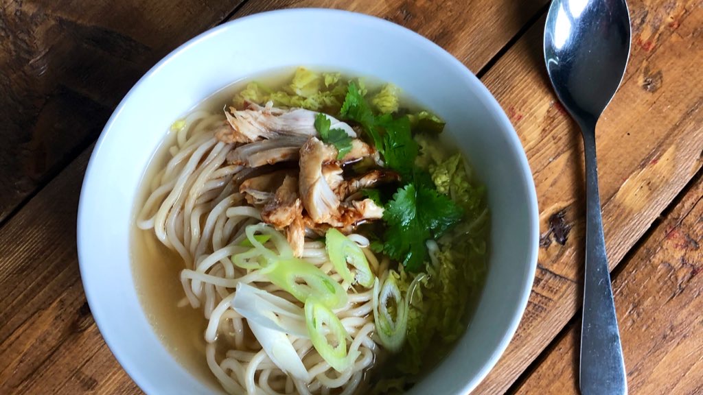 Close up of a bowl of Miso broth with noodles, chicken and spring onions