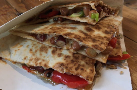 Mixed bean, pepper and cheese quesadillas wrapped in a paper bag on a wooden table