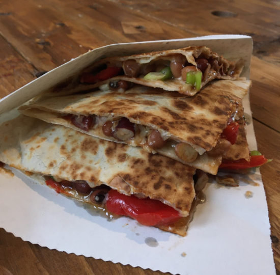 Mixed bean, pepper and cheese quesadillas wrapped in a paper bag on a wooden table