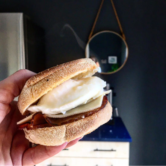 English muffin with poached egg, bacon and cheese, held in a hand