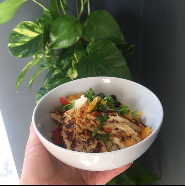 A bowl of warm salad of cous cous, harissa-spiced black chick peas, carrot, coriander and onion, topped with halloumi and greek yoghurt