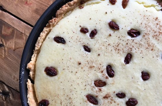 Overhead shot of rice custard tart sprinkled with sultanas, in a pie dish on top of a wooden slated table
