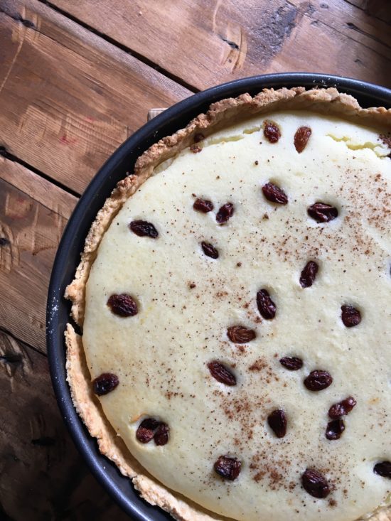 Overhead shot of rice custard tart sprinkled with sultanas, in a pie dish on top of a wooden slated table