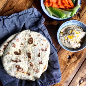 Wooden table with a selection of food - flatbreads, houmous and chopped carrot, cucumber and celery