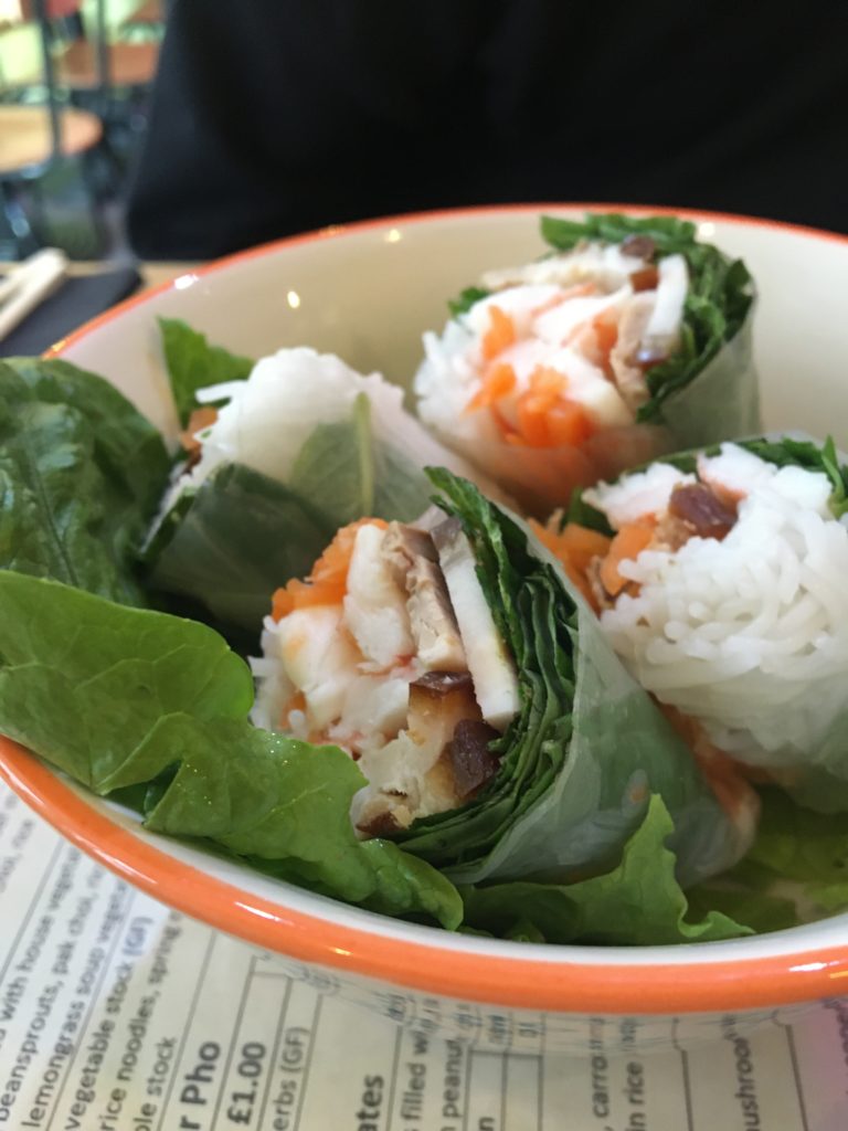 A close-up photo showing the filling of a summer roll - mint, coriander, rice noodles, shredded carrot, pork and prawns