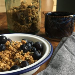 Photo shows an enamel bowl of granola and blueberries in front of a kilner jar of homemade granola