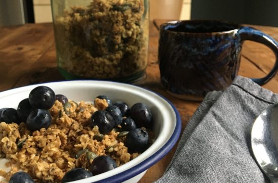 Photo shows an enamel bowl of granola and blueberries in front of a kilner jar of homemade granola